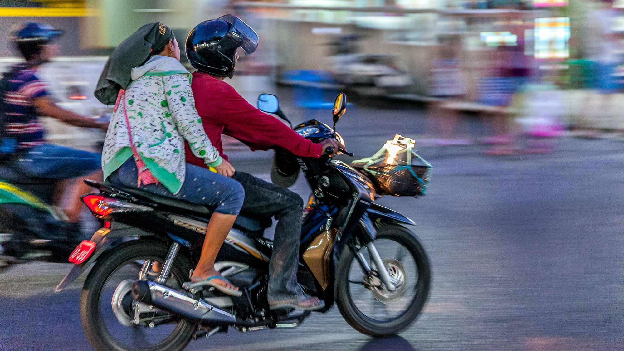 Zwei Personen fahren auf einem Motorrad durch eine belebte Straße in Thailand.